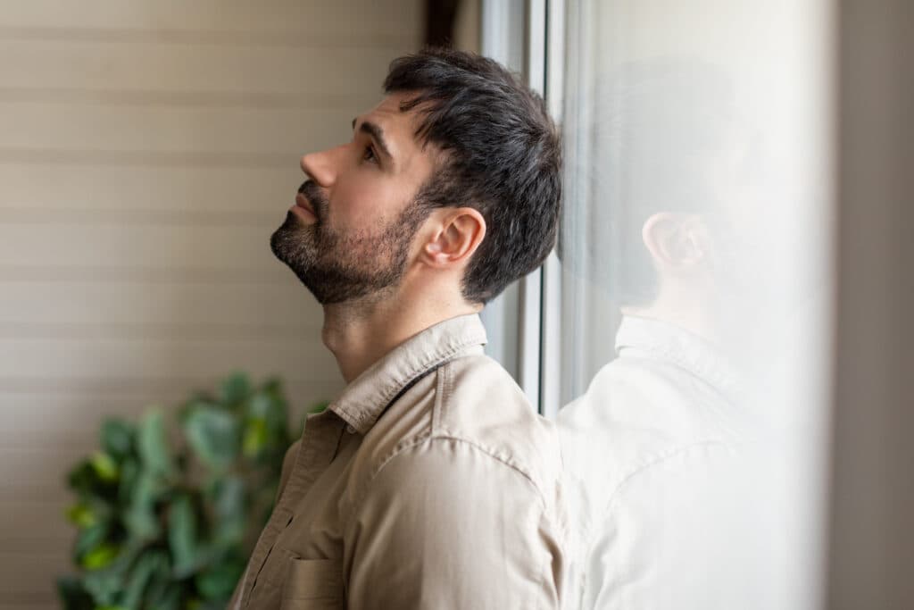 Man standing by a window feeling down